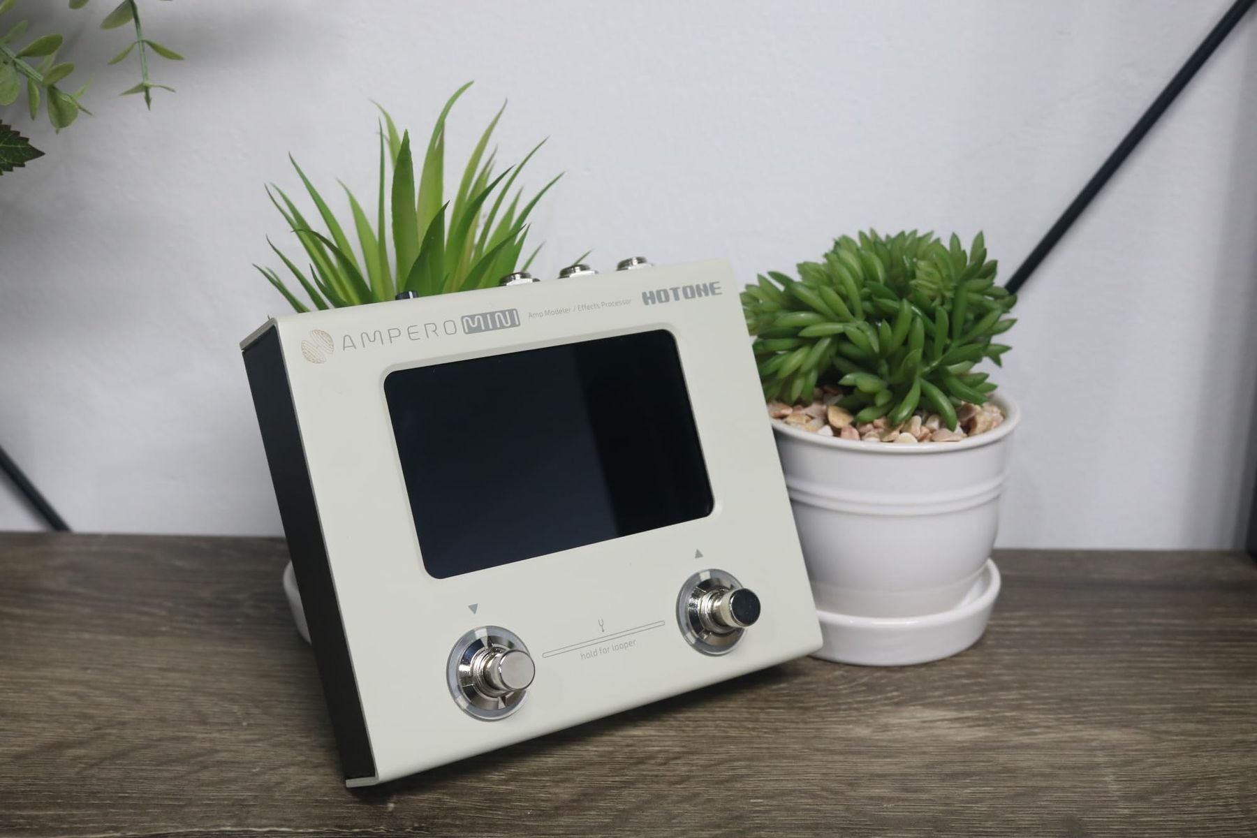 Hotone Ampero Mini MP50VN effects processor — front view on a desk beside a plant — Slide 2 of 9